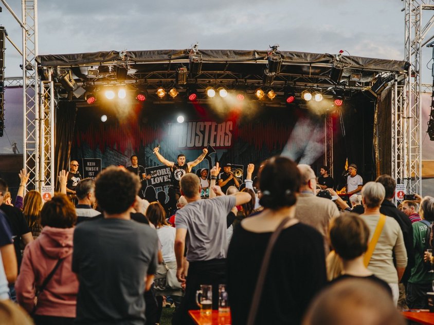 Auf der Bühne im Sportpark spielen The Busters. Viele Menschen stehen vor der Bühne.