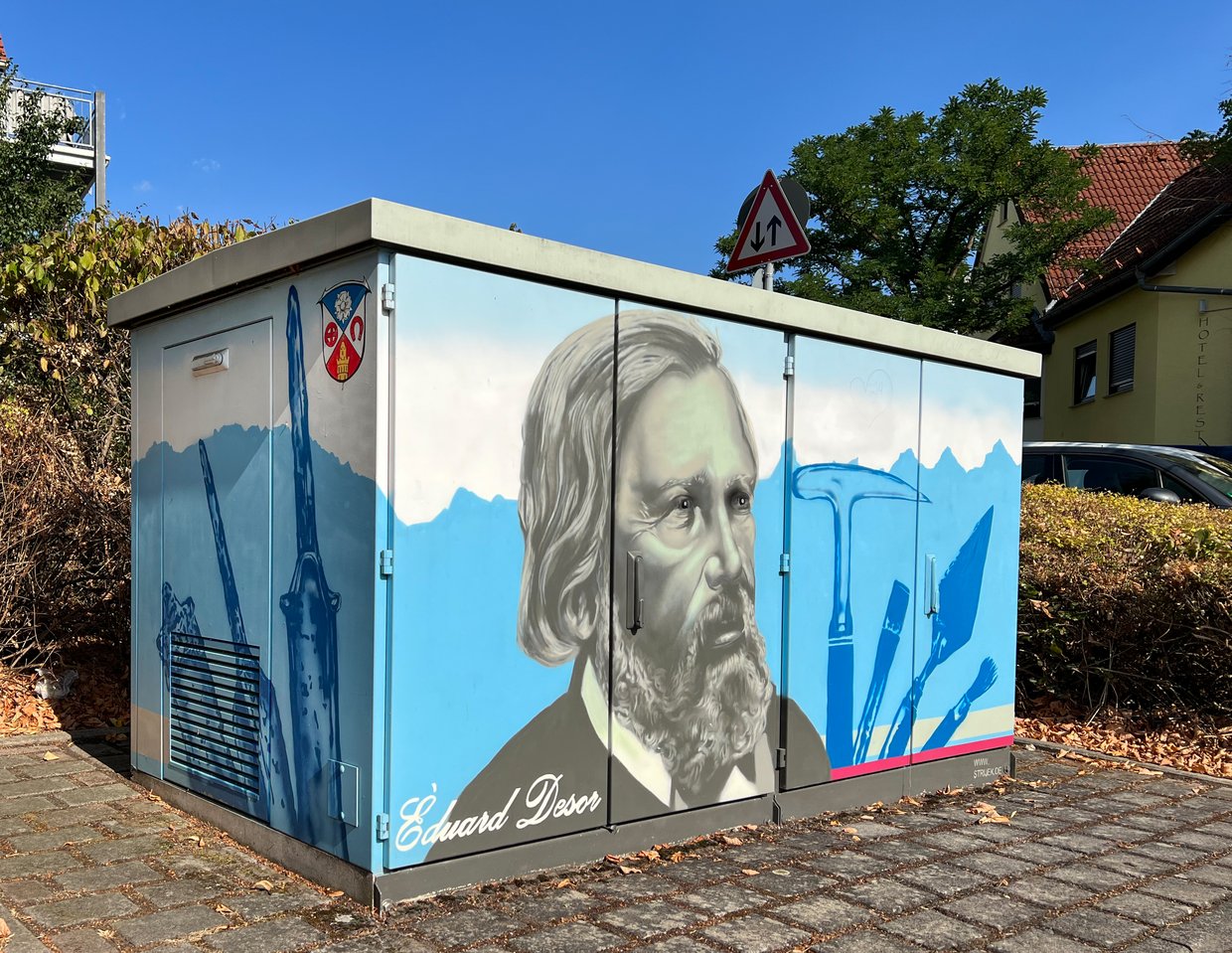 Auf der Darstellung ist das Gesicht von Edouard Désor, eingerahmt von Werkzeugen, zu sehen.