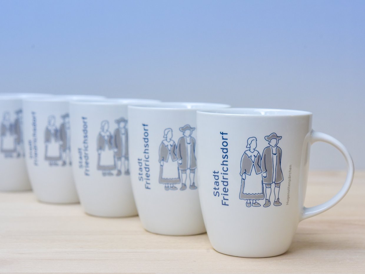 Auf der Darstellung sind fünf weiße Porzellantassen in einer Reihe zu sehen, die mit dem Hugenottenpärchen verziert sind.