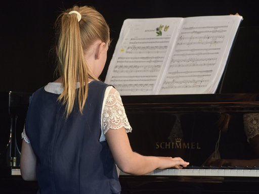 Auf dem Bild ist ein junges Mädchen am Klavier spielend zu sehen.