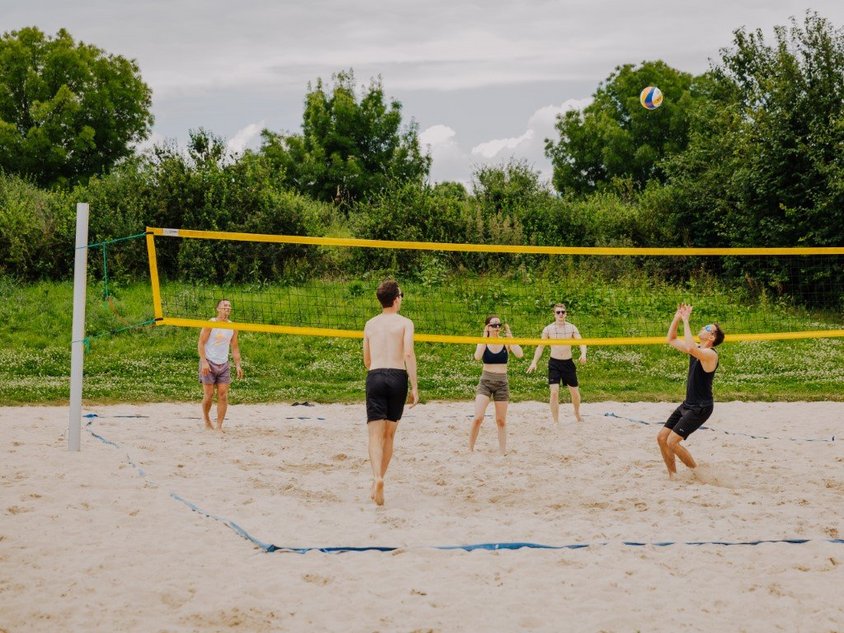 Das Bild zeigt Menschen, die Beachvolleyball im Sportpark spielen.