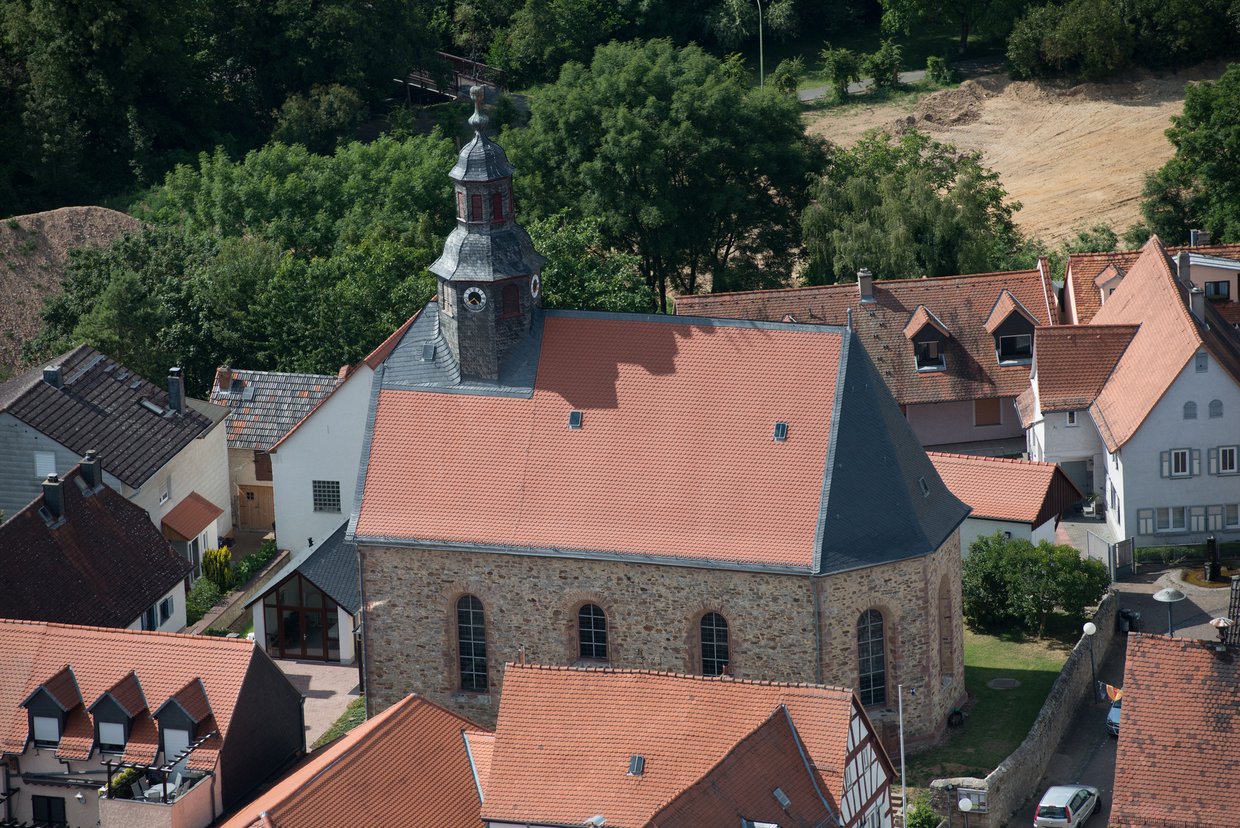 Auf der Darstellung ist eine Luftaufnahme des alten Ortskerns von Burgholzhausen zu sehen, in der Mitte die Evangelische Kirche Burgholzhausen aus Feldstein.