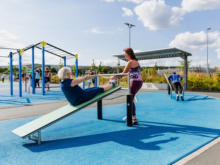 Auf dem Bild nutzen Menschen Street-Workout-Geräte und machen zum Beispiel Liegestütze.