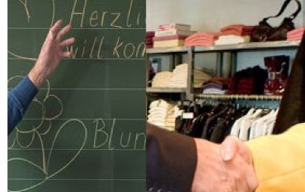 Tafel mit „Herzlich willkommen“ beschriftet, Hände schütteln sich, im Hintergrund ein Regal mit Kleidung, Taschen und Büchern