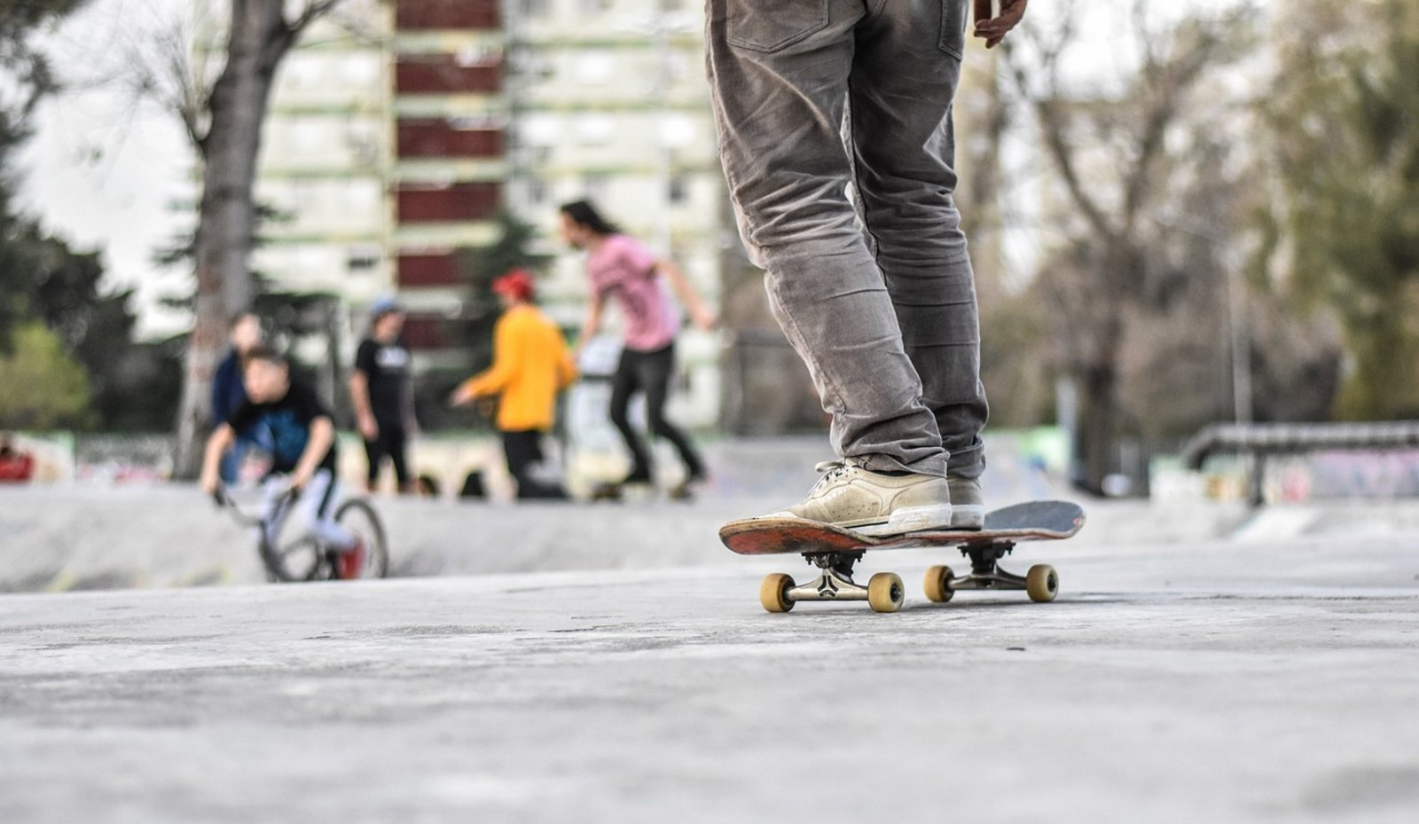 Im Vordergrund ist ein Skateboardfahrer, im Hintergrund Jugendliche im Skatepark zu sehen.