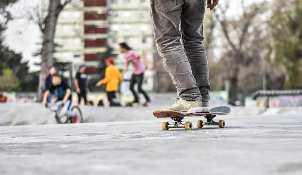Im Vordergrund ist ein Skateboardfahrer, im Hintergrund Jugendliche im Skatepark zu sehen.
