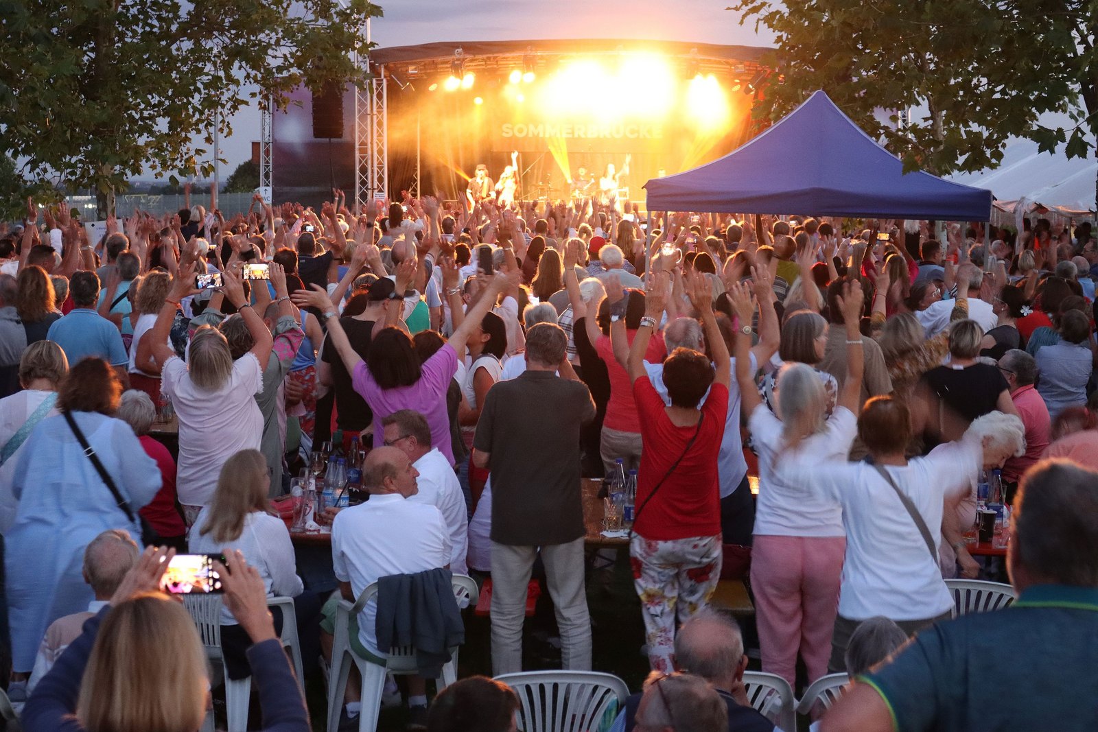 Das Foto zeigt viele Menschen, die vor der Bühne im Sportpark stehen und die Arme in die Luft strecken.