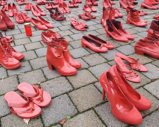 Rot lackierte Frauenschuhe stehen auf einem Gehweg.
