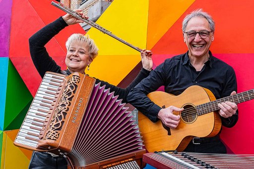 Auf dem Bild sind die beiden Musiker des Duos Kaleido mit Instrumenten in der Hand vor einer bunten Wand zu sehen.