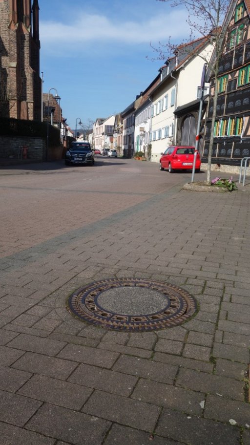 Symbolbild für die Kanalsanierungsarbeiten. Zu sehen ist ein Kanaldeckel uf einer gepflasterten Straße.