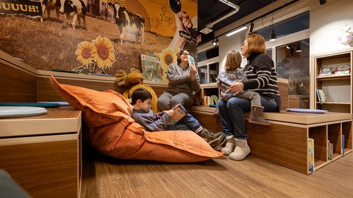 Erwachsene und Kinder sitzen in der Stadtbücherei und zeigen sich Bücher