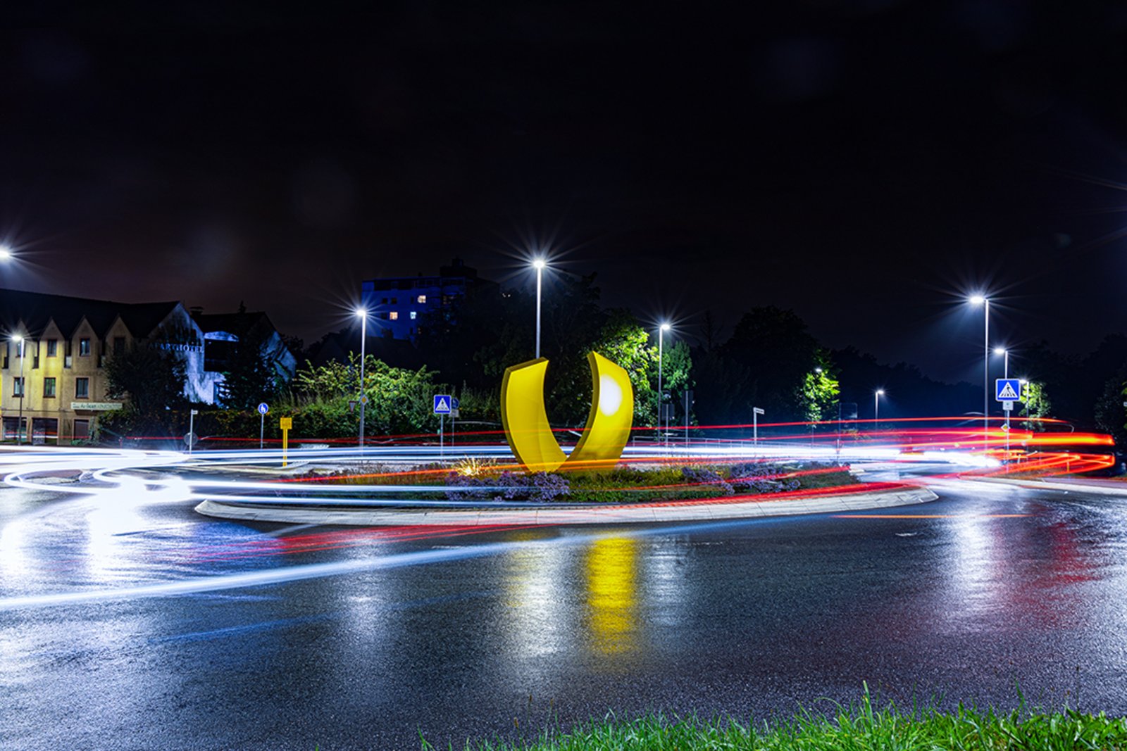 Zu sehen ist einer der Friedrichsdorfer Verkehrskreisel in der Dunkelheit mit den Autolichtern der vorbeifahrenden PKWs.