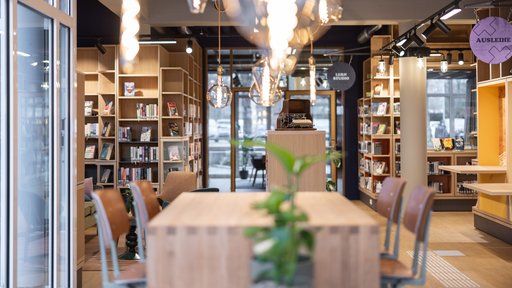 Das Bild von der Stadtbücherei zeigt Bücherregale und einen Tisch mit Stühlen.