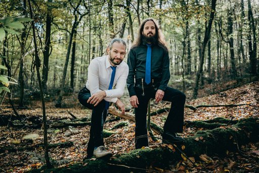 Auf dem Bild sind die beiden Musiker von Stout von Wald umgeben zu sehen.