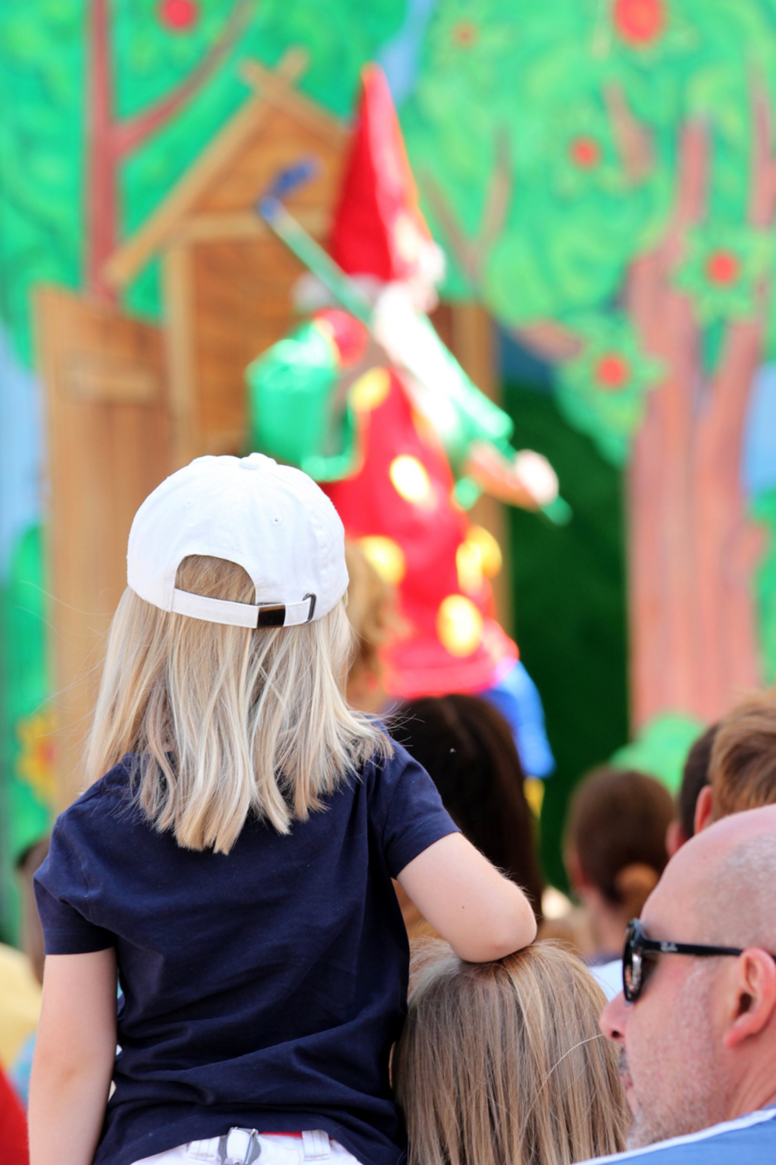 Auf der Darstellung ist ein Kind von hinten zu sehen, das ein Theaterstück auf der Bühne verfolgt.