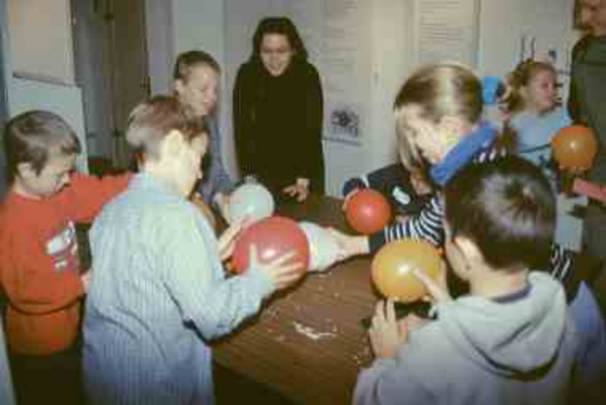 Erfinderwerkstatt Kinder und Erwachsene stehen um einen Tisch herum und experimentieren mit einem Luftballon