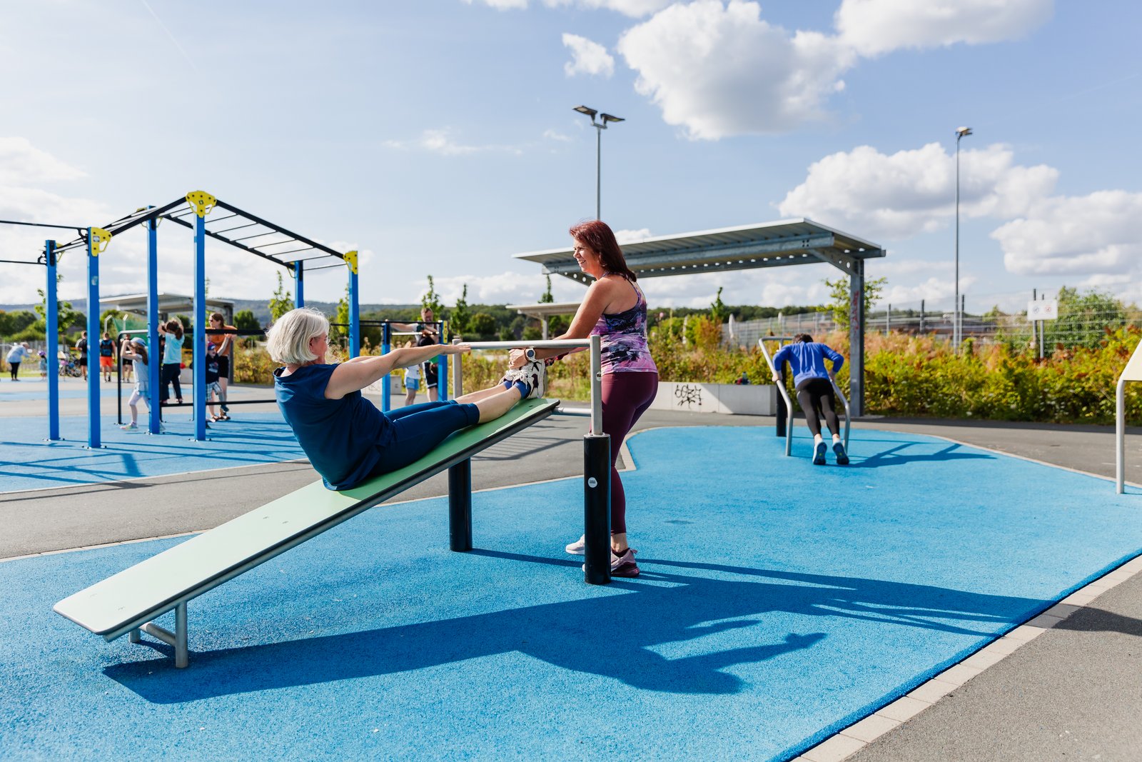 Auf dem Bild nutzen Menschen Street-Workout-Geräte und machen zum Beispiel Liegestütze.