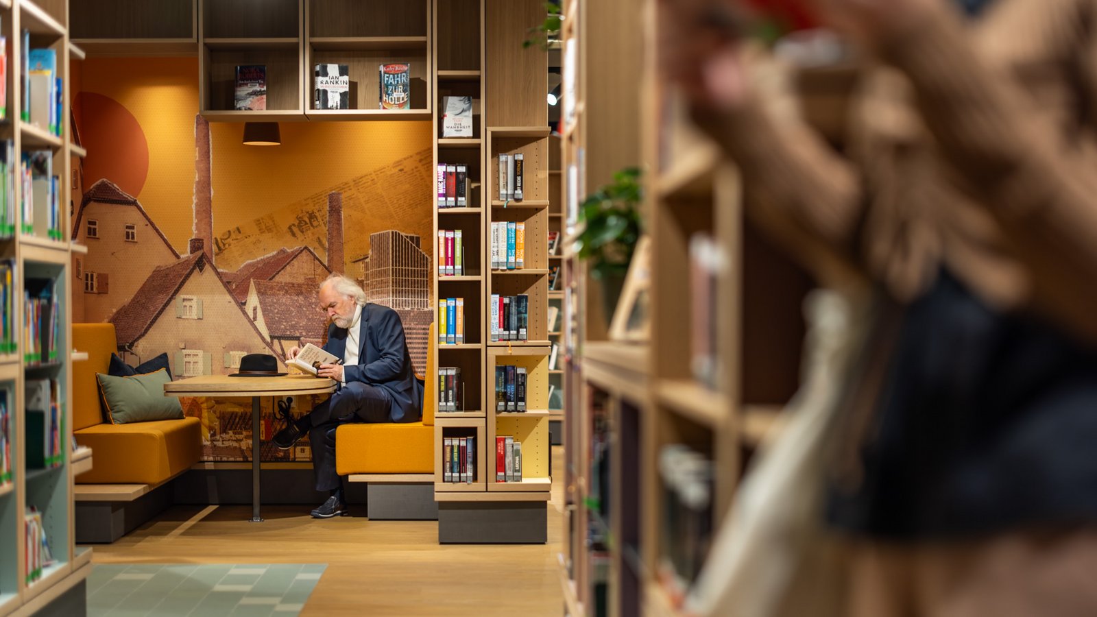 Ein „Kokon“ zum Zurückziehen Ein Mann sitzt lesend in einer Kabine. Die Kabine ist mit zwei orangen Sofas und einem Tisch ausgestattet.