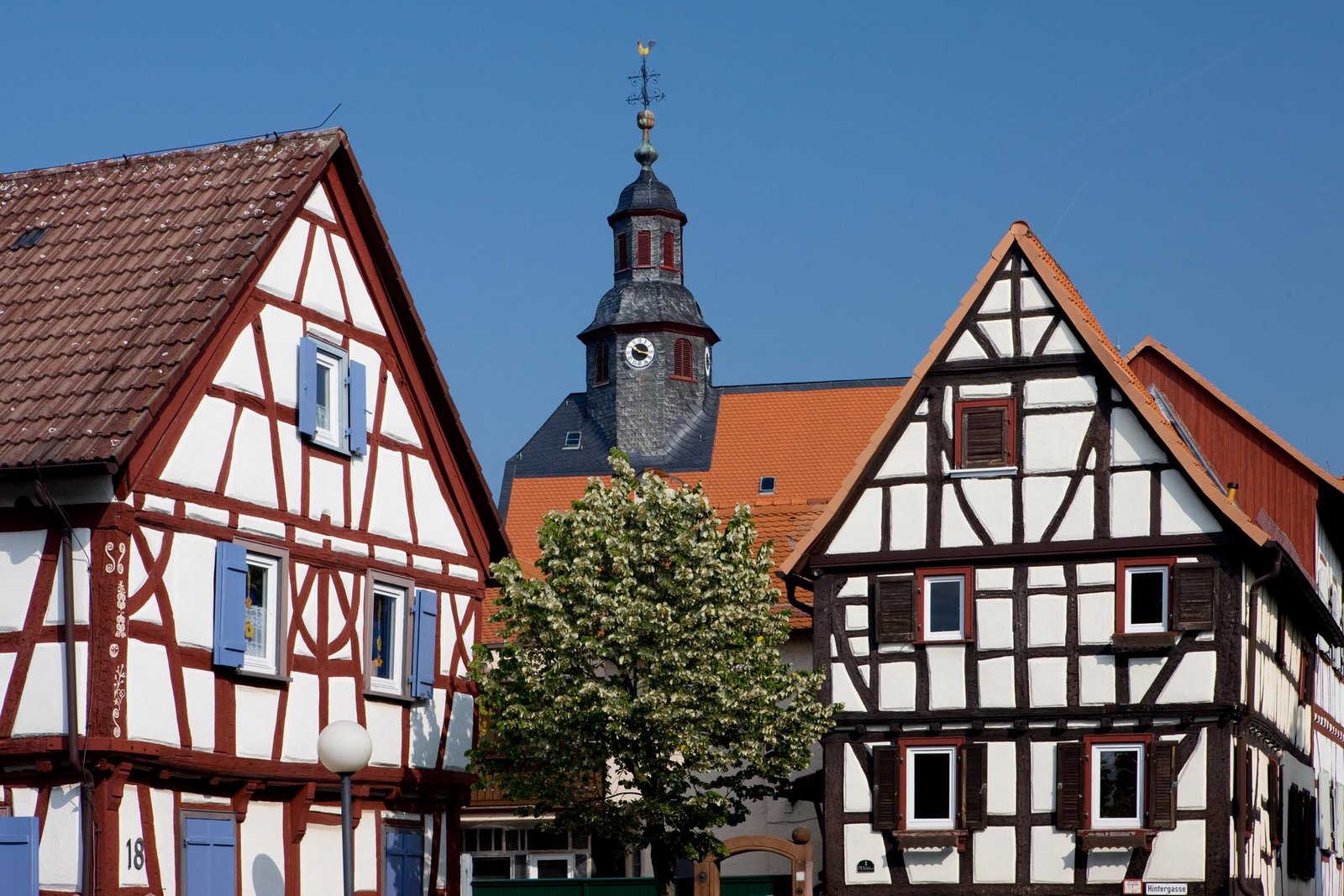 Auf der Darstellung sind liebevoll restaurierte Fachwerkhäuser zu sehen, im Hintergrund die Evangelische Kirche Burgholzhausen.